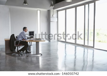 Full length side view of a man sitting at desk in empty office