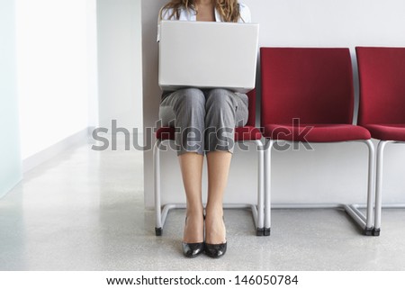 Lowsection of a female executive using laptop on chair in corridor