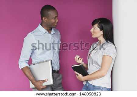 Casual multiethnic young male and female executives talking against pink wall