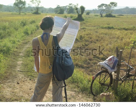 Rear view of a young woman standing in field with backpack and map