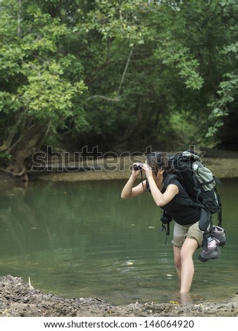 Side view of a young woman in water with backpack looking through binoculars