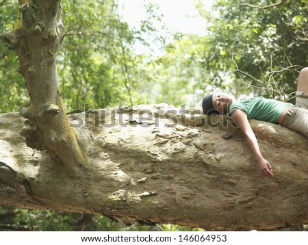 Side view of a young mixed race woman resting on large tree branch in forest
