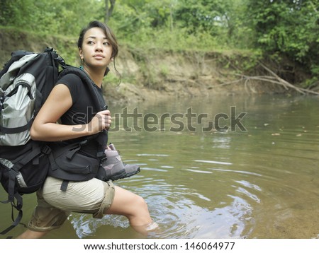 Side view of a young mixed race woman carrying backpack while walking in forest water