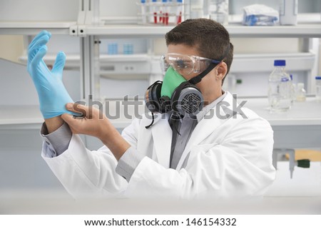 Male scientist in a gas mask while putting on rubber glove in laboratory
