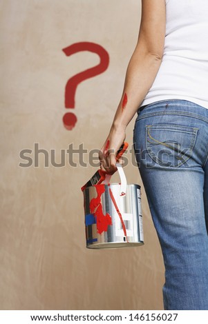 Rear view midsection of a woman holding paint can with painted question mark on wall