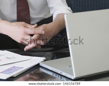 Closeup of businessman sitting on sofa by laptop with hands clasped