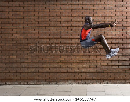 Side view of an African American man jumping against brick wall