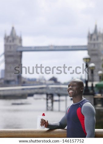 Smiling young African American man with water bottle in front of Tower Bridge in England