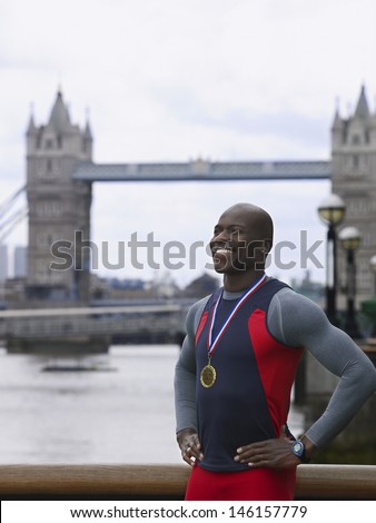 Smiling young African American man wearing medal in front of Tower Bridge in England