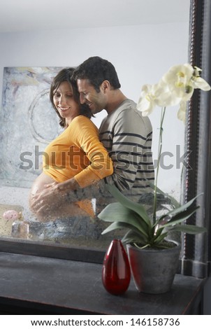 Side view of reflection of a man embracing pregnant woman from behind in bedroom
