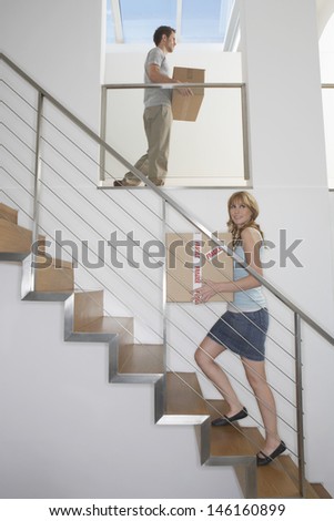 Side view of a young couple carrying boxes upstairs in new home