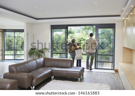 Rear view of parents and daughter looking through patio door in new home