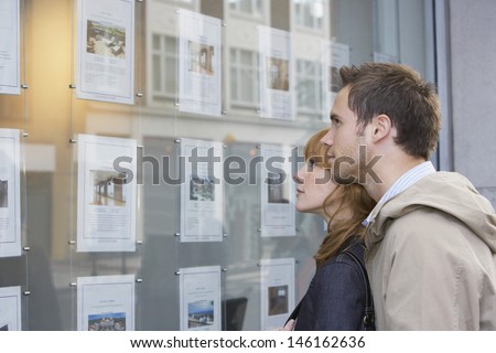 Side view of a young couple looking at window display at real estate office