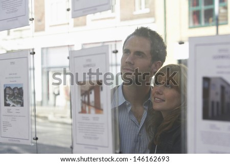 Closeup of a young couple looking through window at estate agents