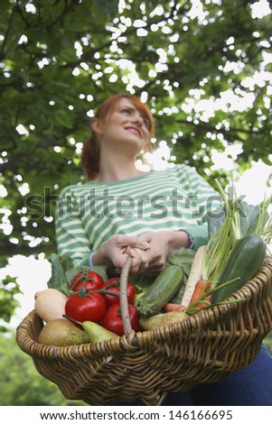 Low angle view of a smiling woman holding vegetable basket outdoors