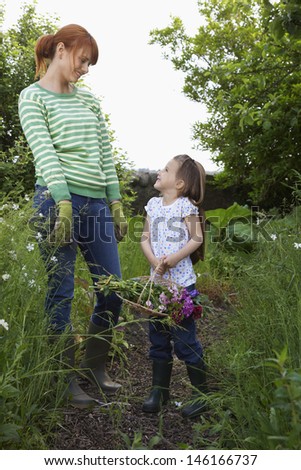 Full length of a smiling woman and daughter with flower basket in garden