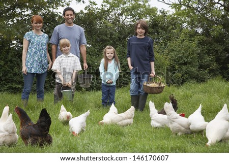 Parents with three children feeding hens on grassland