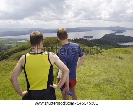 Rear view of two men standing on hill against the lake