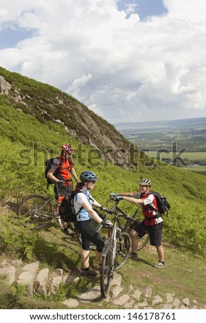 Happy three cyclists with bikes against lush landscape and clouds