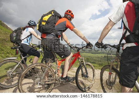 Three cyclists with bikes on track looking at landscape