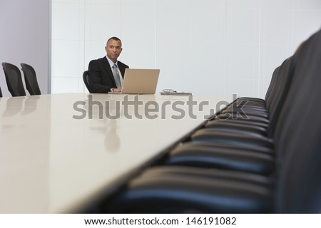Serious middle aged businessman with laptop in board room