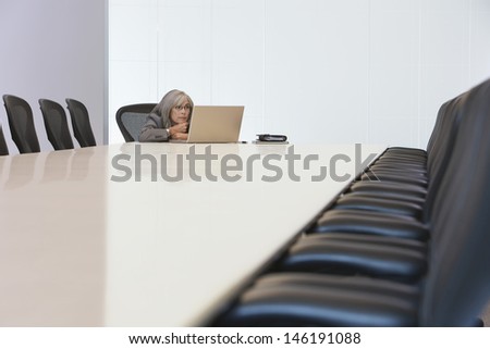 Bored middle aged businesswoman looking at laptop screen in board room
