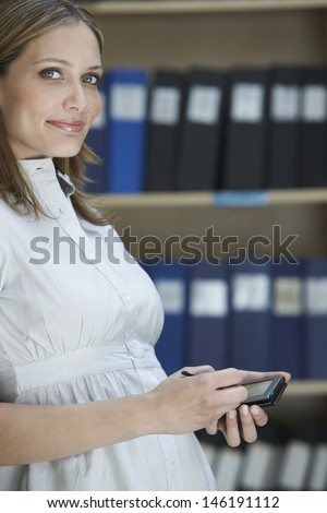 Portrait of a smiling young female office worker with palm top in file storage room