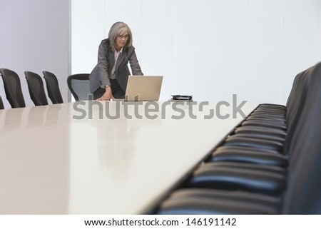 Middle aged businesswoman looking at laptop screen in board room