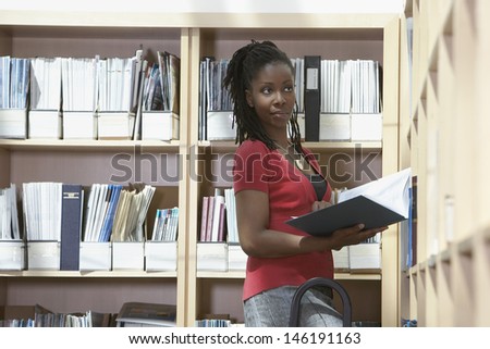 Side view of a female office worker standing on ladder in file storage room