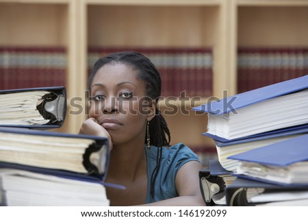 Closeup of a female office worker sitting behind stacks of documents in office