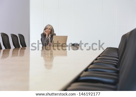 Middle aged businesswoman looking up by laptop in board room