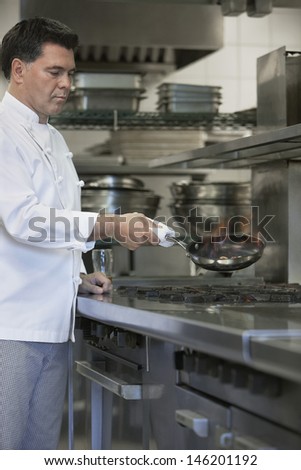 Side view of a male chef cooking food using frying pan in kitchen