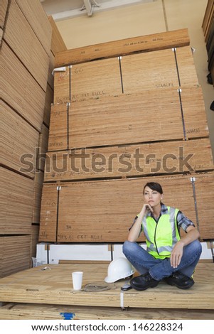Pensive female industrial worker sitting cross-legged on wooden planks