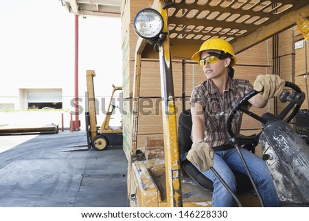 Female industrial worker looking away while driving forklift truck
