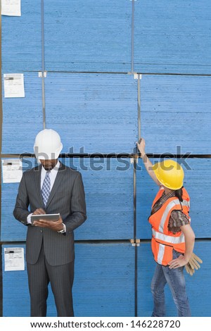 African American male engineer working on tablet PC while female industrial worker checking wooden planks
