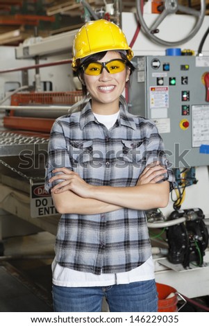 Portrait of happy Asian female industrial worker with machinery in background