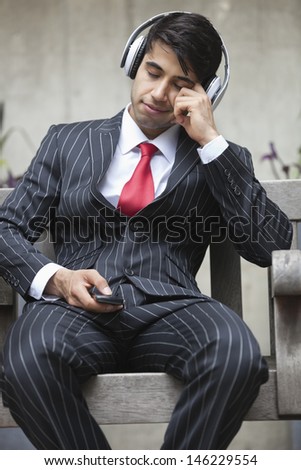 Young Indian businessman with eyes closed listening music on headphones