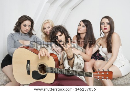 Young male guitarist with cool gesture surrounded by female friends