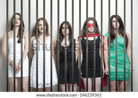 Woman in superhero costume with female friends standing behinds prison bars