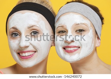Portrait of two happy women with face pack on their faces over yellow background