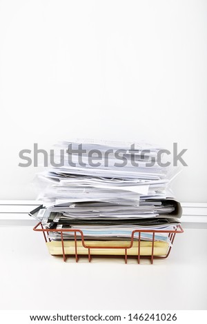 Documents overflowing in desk tray against white wall