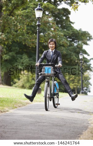 Portrait of young businessman riding bicycle with legs kicked out