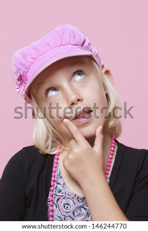 Thoughtful young girl wearing cap with finger on chin over pink background