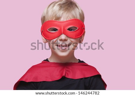 Portrait of a happy boy in superhero costume over pink background