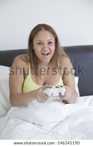 Young pregnant playing video game with remote control in bed