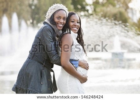 Portrait of happy young woman embracing pregnant woman from behind