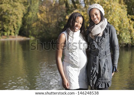 Portrait of happy young female friend embracing pregnant woman from behind
