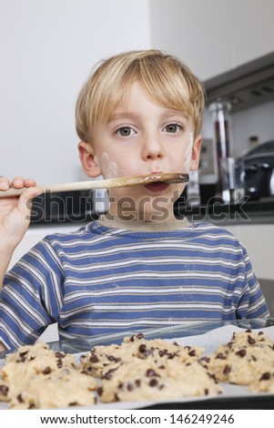 Portrait of young boy tasting spatula mix with cookie batter