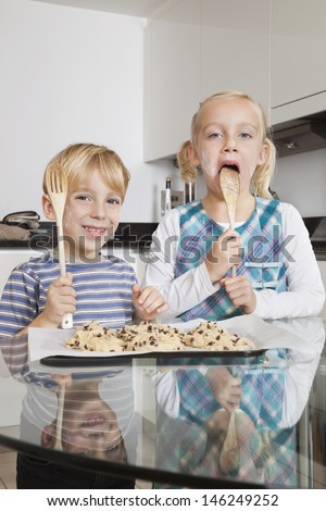 Portrait of happy boy with sister tasting spatula mix with cookie batter in kitchen