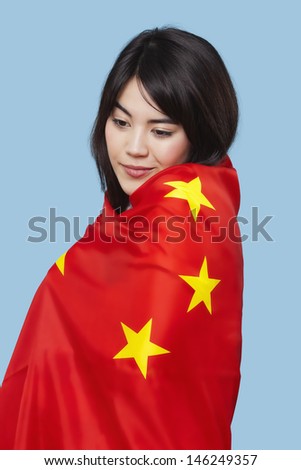 Patriotic young woman wrapped in Chinese flag over blue background